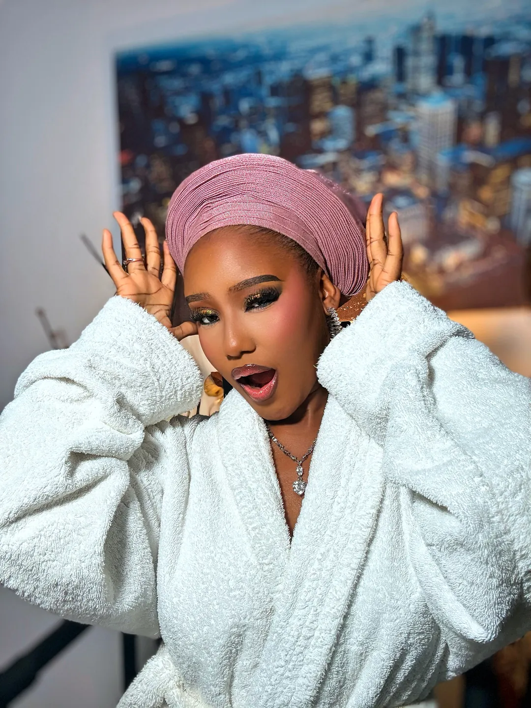 Blush gele and white robe, hands raised beside her face