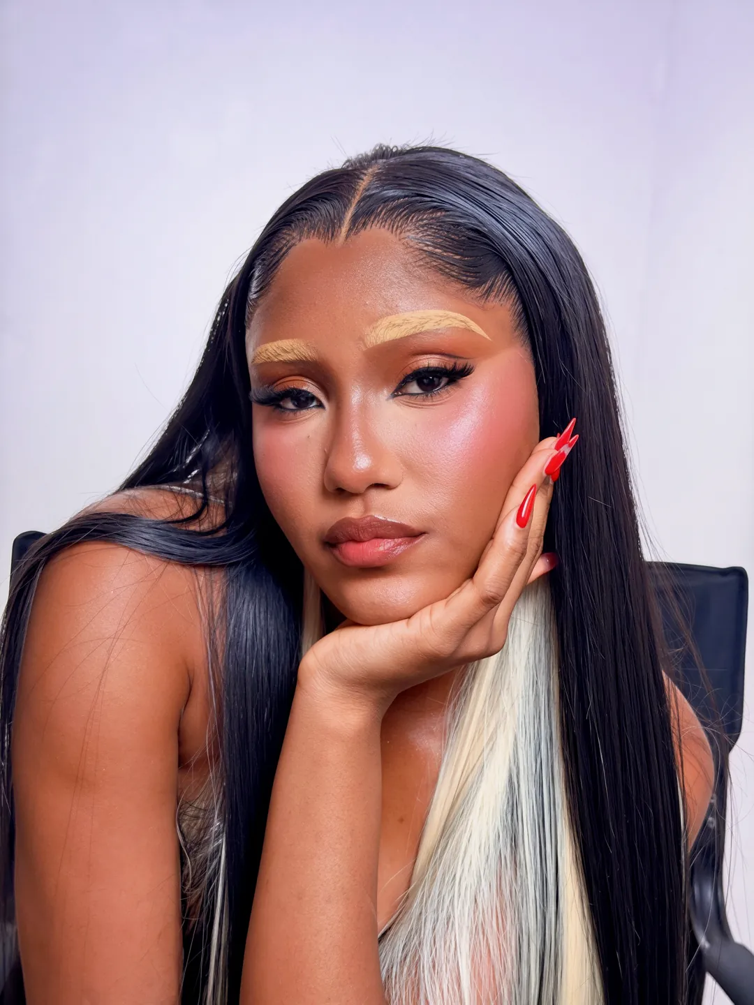 Chin resting on her hand, two-tone hair and bold makeup